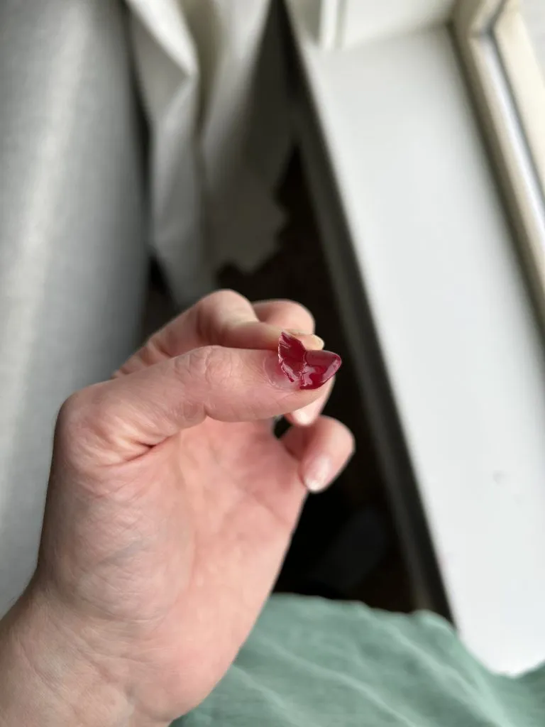 Gel polish peeling off cranberry-colored nails, a common issue with DIY gel manicures without proper prep or base coat.