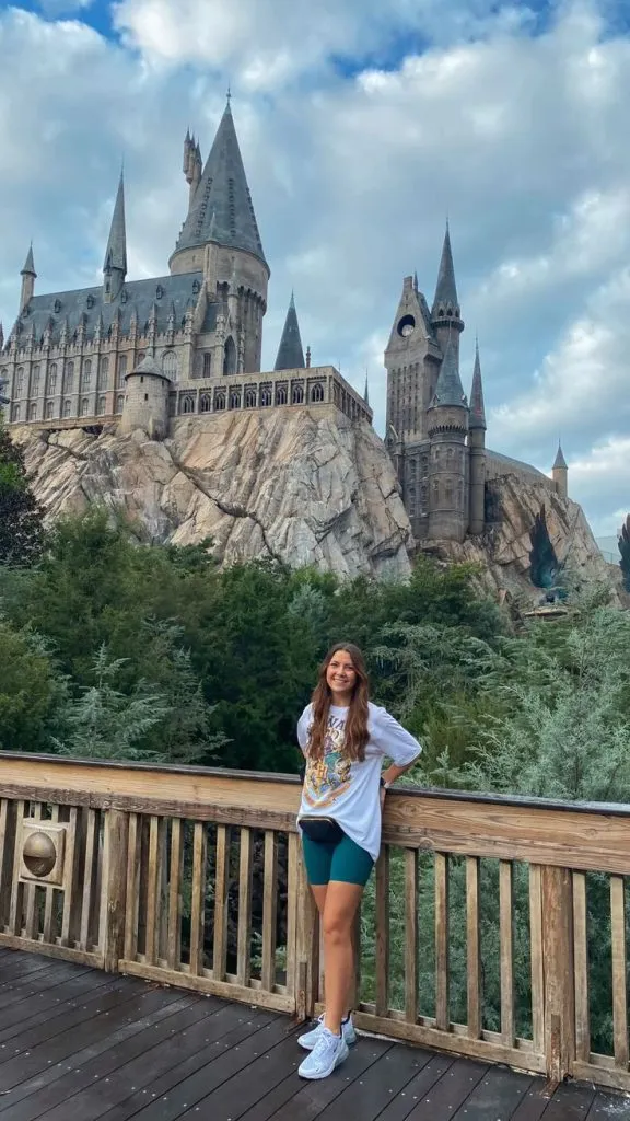 Woman posing in front of Hogwarts at Universal Studios wearing a Harry Potter t-shirt, green biker shorts, sneakers, and a black waist bag.