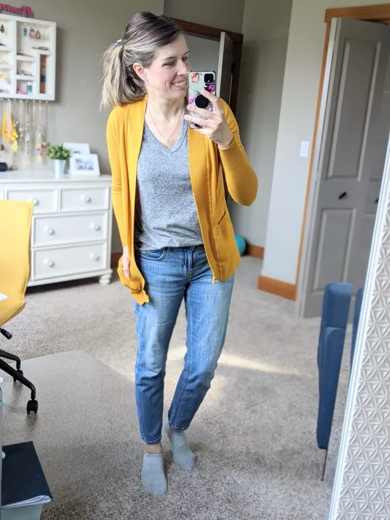 Woman in straight leg jeans, gray tee, and mustard yellow cardigan posing indoors.
