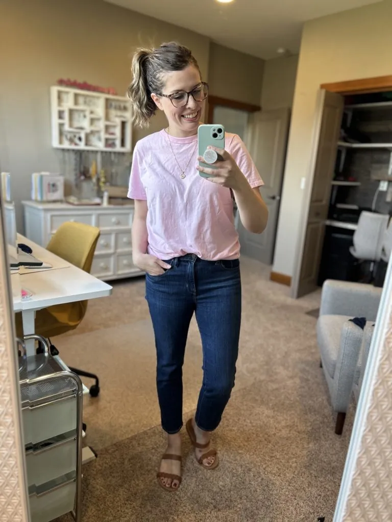 Woman wears dark wash straight jeans with pink tee and brown sandals for a casual summer look
