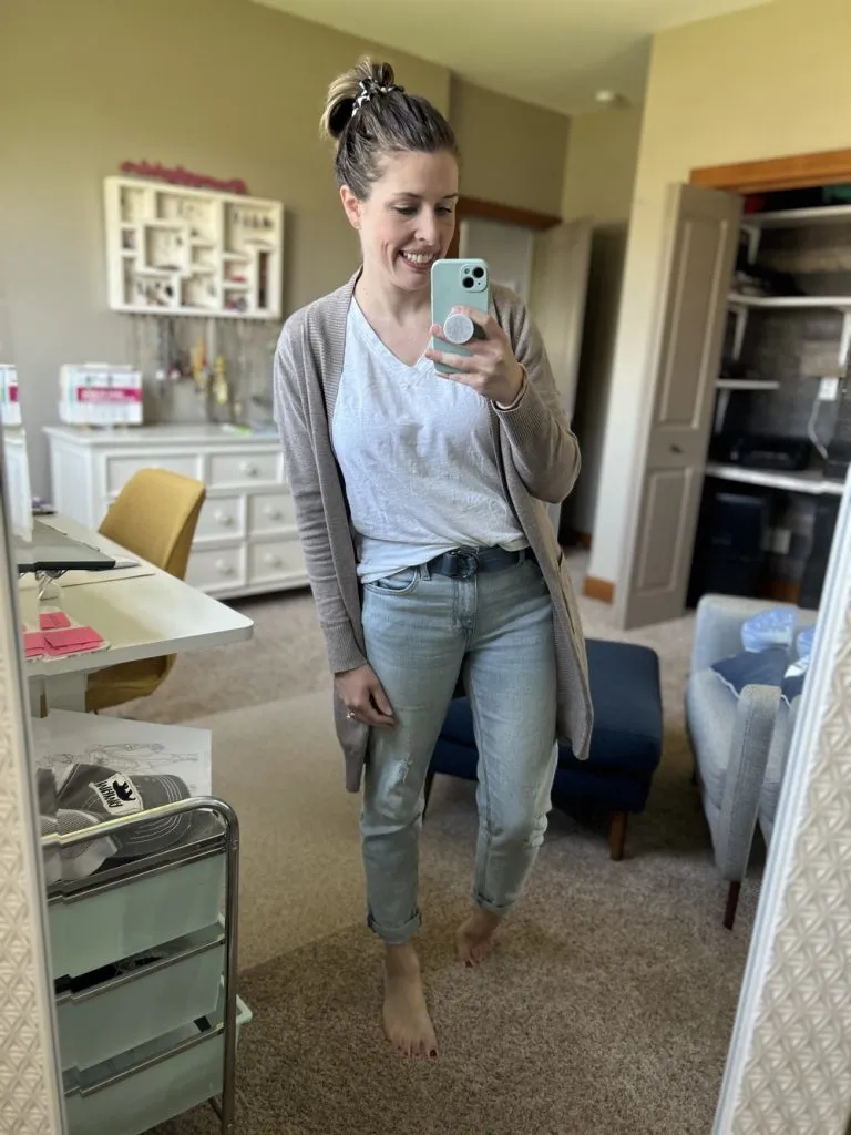 Woman wearing straight leg jeans with white tee and beige cardigan, smiling in mirror.