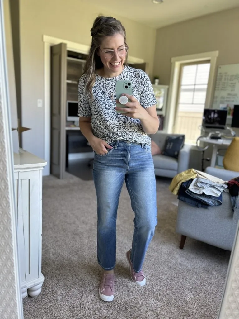 Woman in floral tee and relaxed straight jeans with pink sneakers posing for a mirror selfie