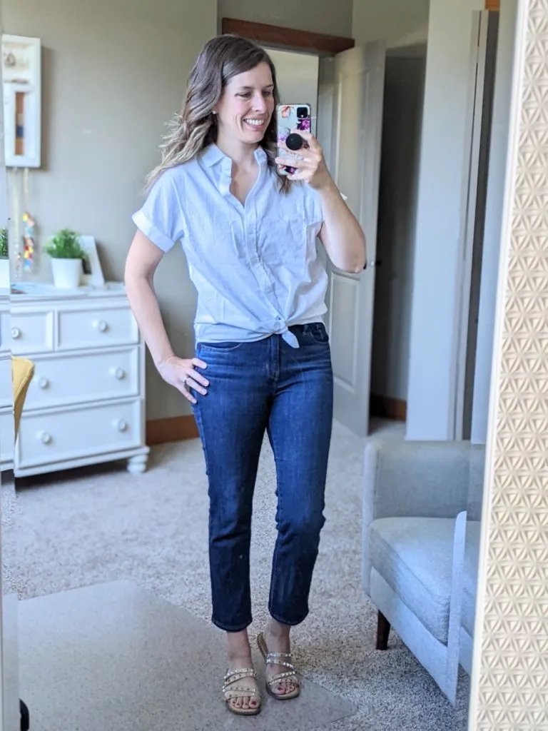 Woman wears short sleeve button-up and dark cropped slim straight jeans with shiny flat sandals indoors