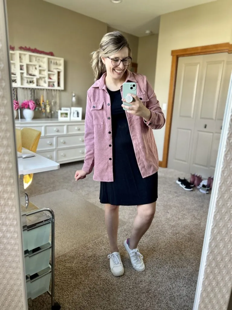 Woman in black dress with pink jacket and sneakers for casual everyday fall outfit.