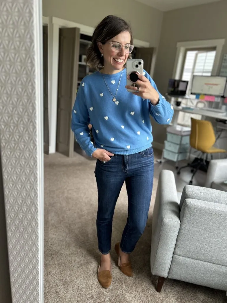 Woman wearing blue sweater with heart print, dark jeans, and flats for a casual fall outfit.