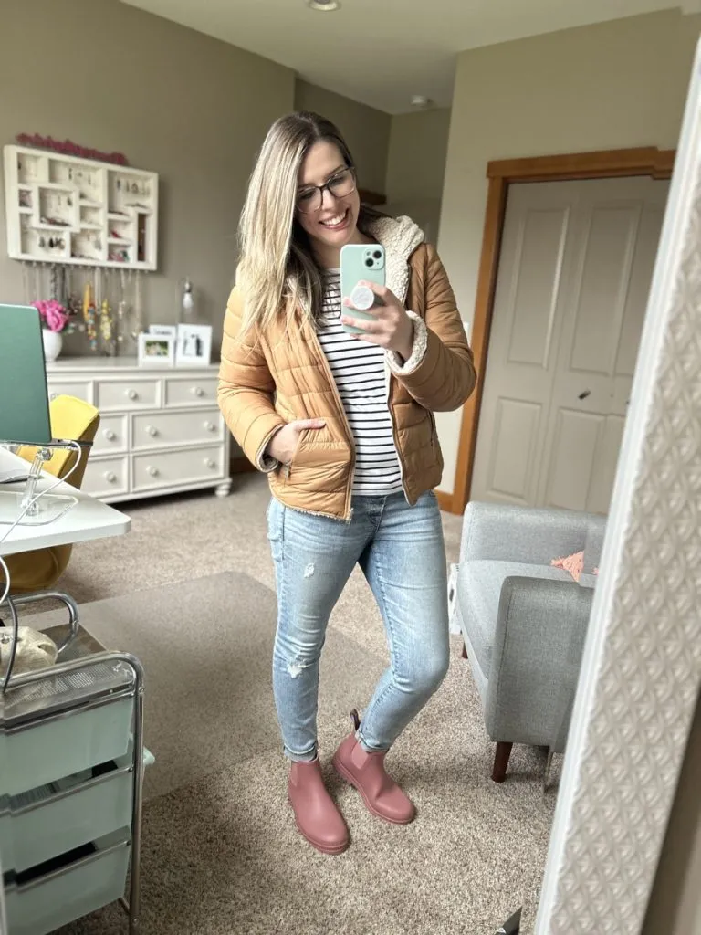 Woman in striped tee, puffer jacket, jeans, and pink rain boots for casual fall outfit.