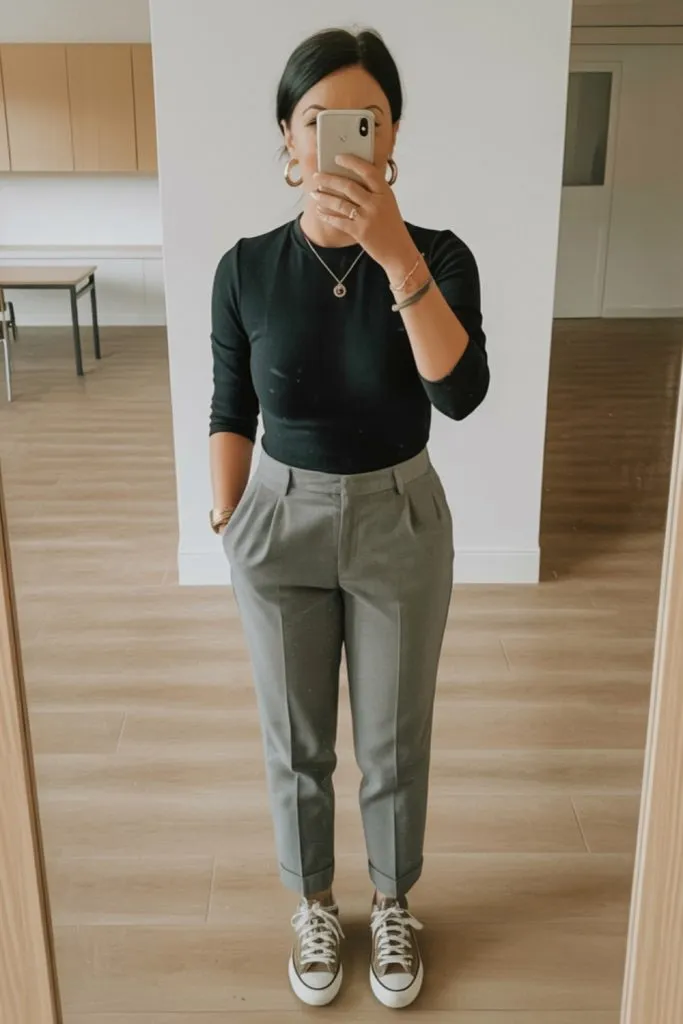 Woman wearing black fitted top, gray pleated trousers, and Converse sneakers for a trendy fall teacher outfit.