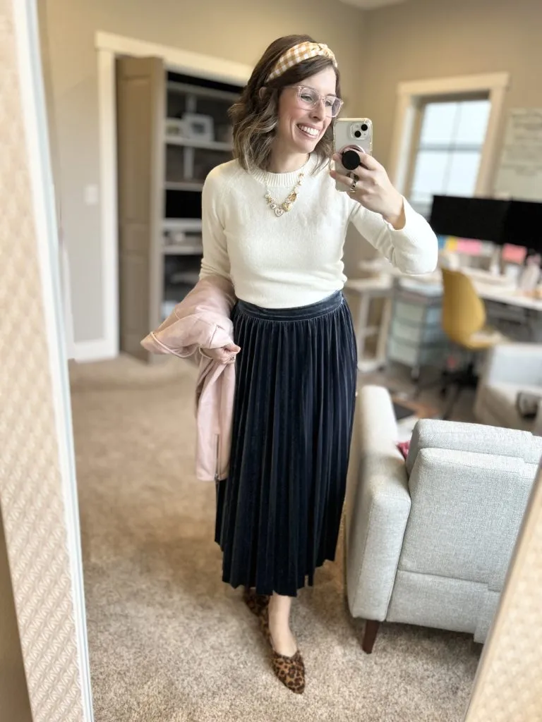 Woman wearing cream sweater with black pleated skirt and flats, modest christmas outfit for women over 40