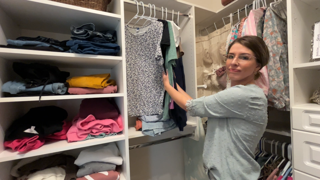 Woman holding small capsule wardrobe pieces in closet, testing mix and match outfits