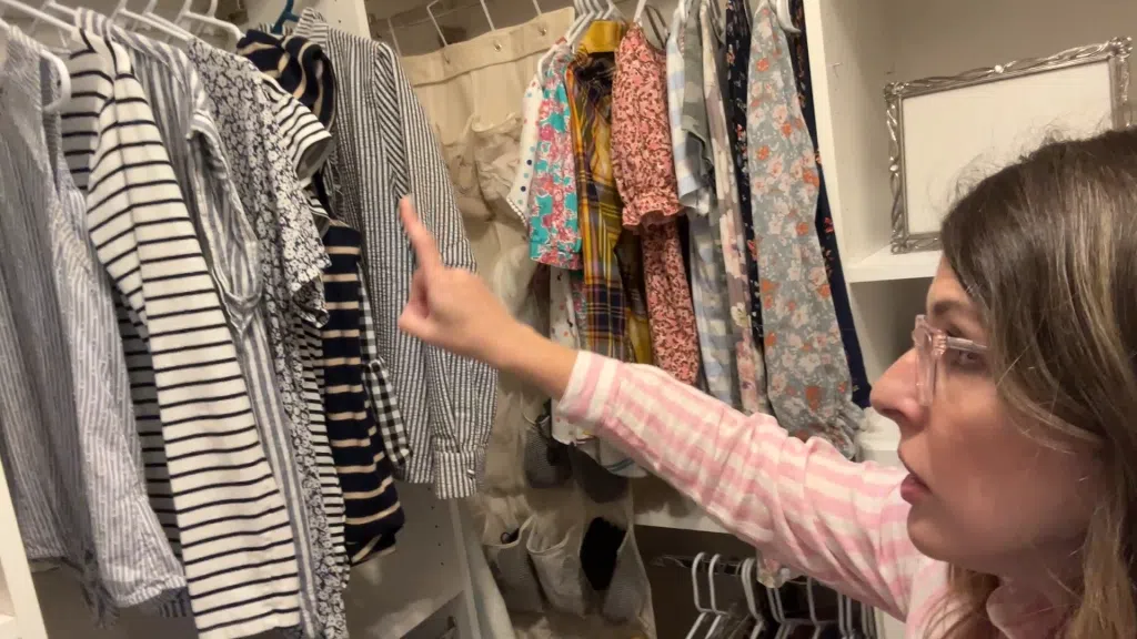 Woman organizing closet by category and color with folded jeans and striped tops on white shelves