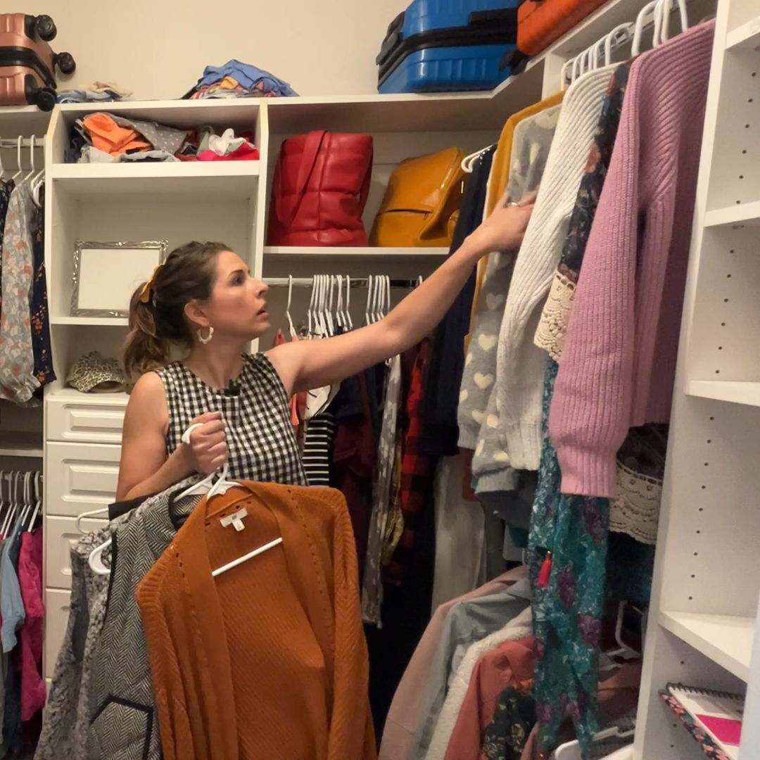Woman rotating seasonal clothes in closet with sweaters and dresses on hangers