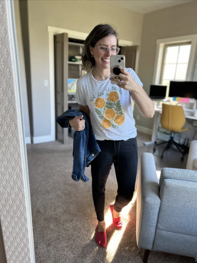 Woman wearing black joggers with a graphic tee and denim jacket in a mirror selfie
