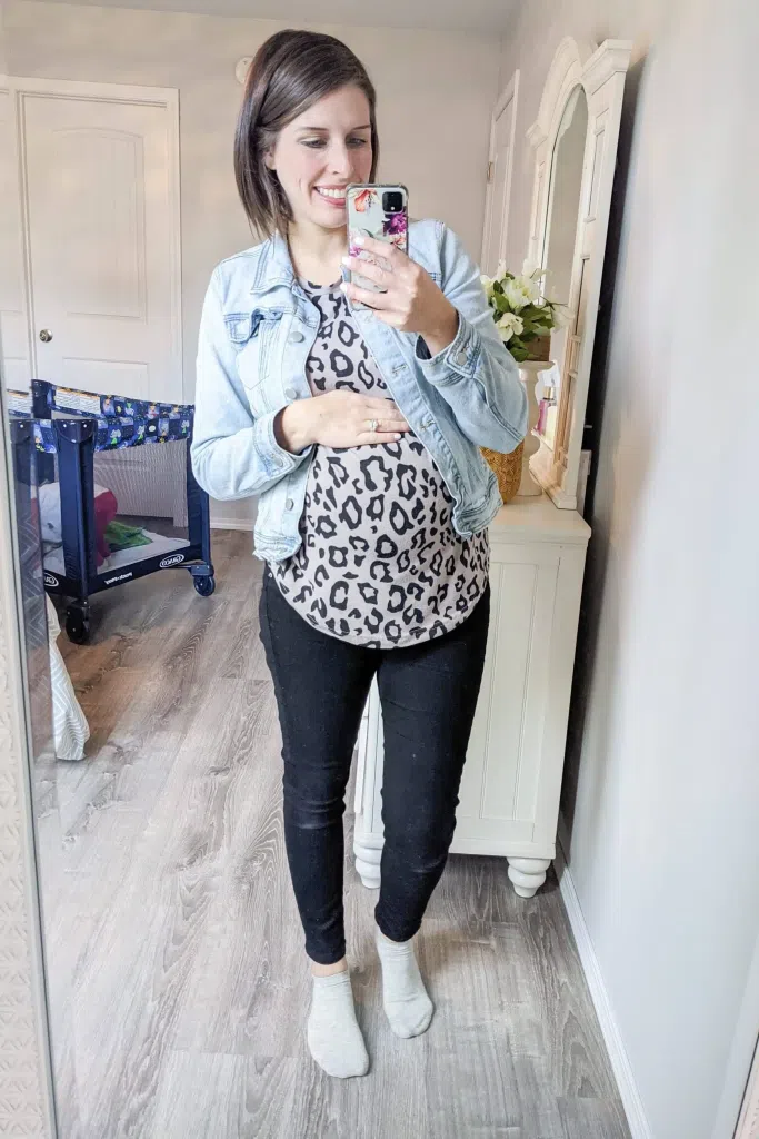 Woman wearing black leggings with a printed top and denim jacket in a mirror selfie