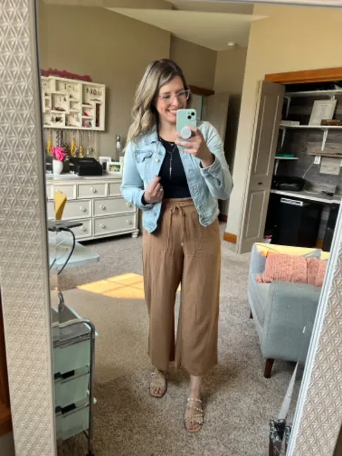Woman wearing a cropped denim jacket with brown wide leg pants and sandals indoors