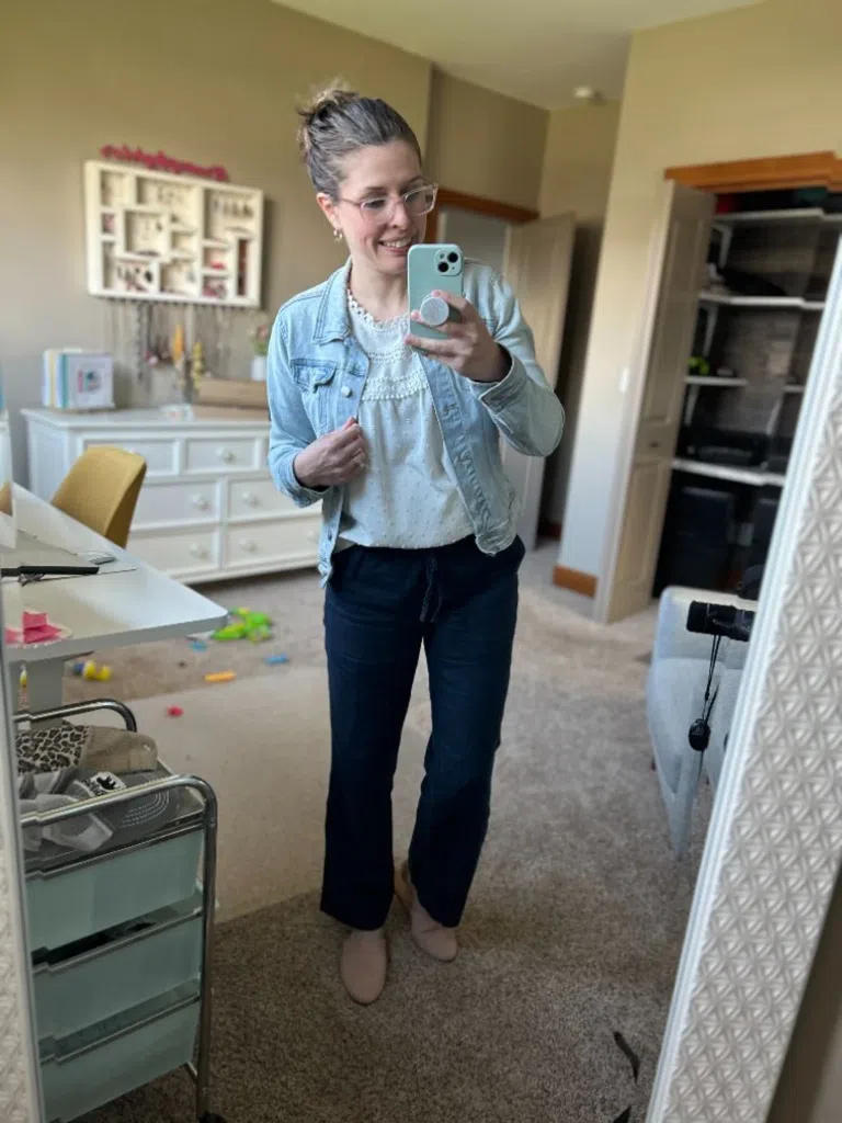 Woman wearing dark linen pants with a light blouse and denim jacket in a mirror selfie
