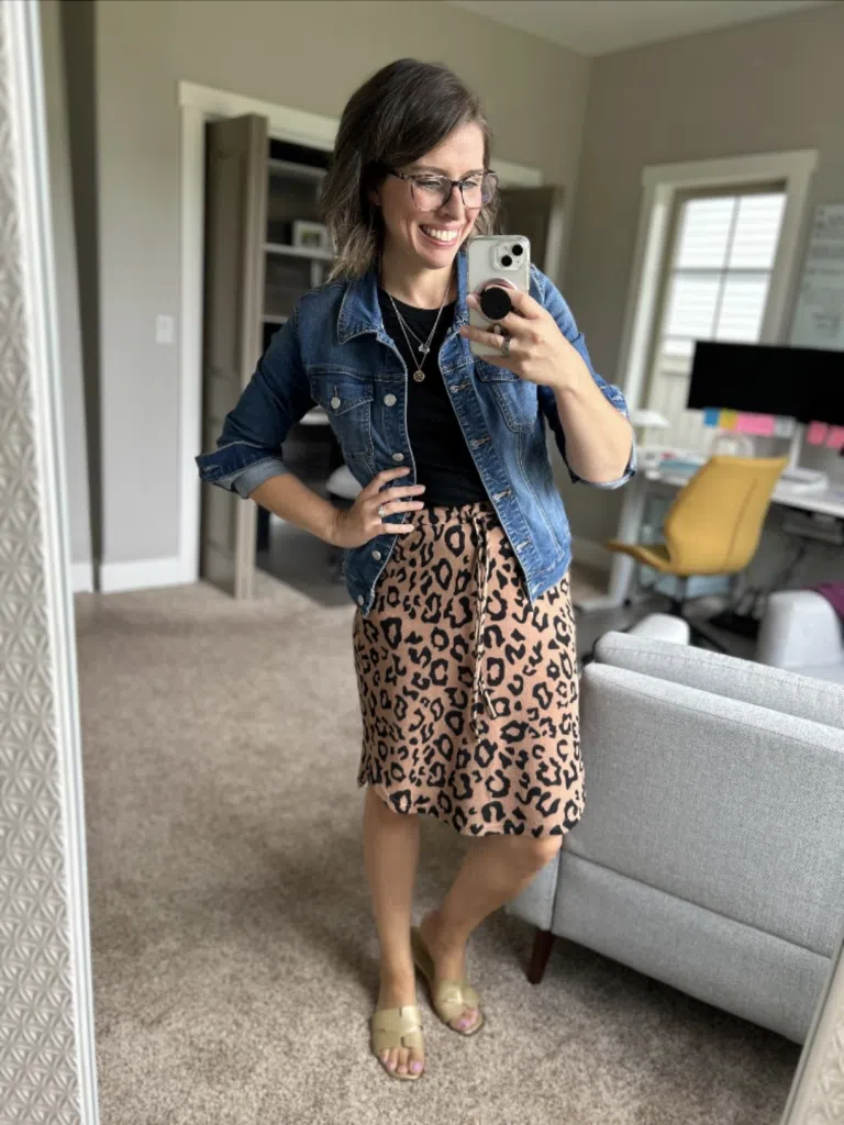 Woman wearing a leopard print skirt with a black top and denim jacket in a mirror selfie