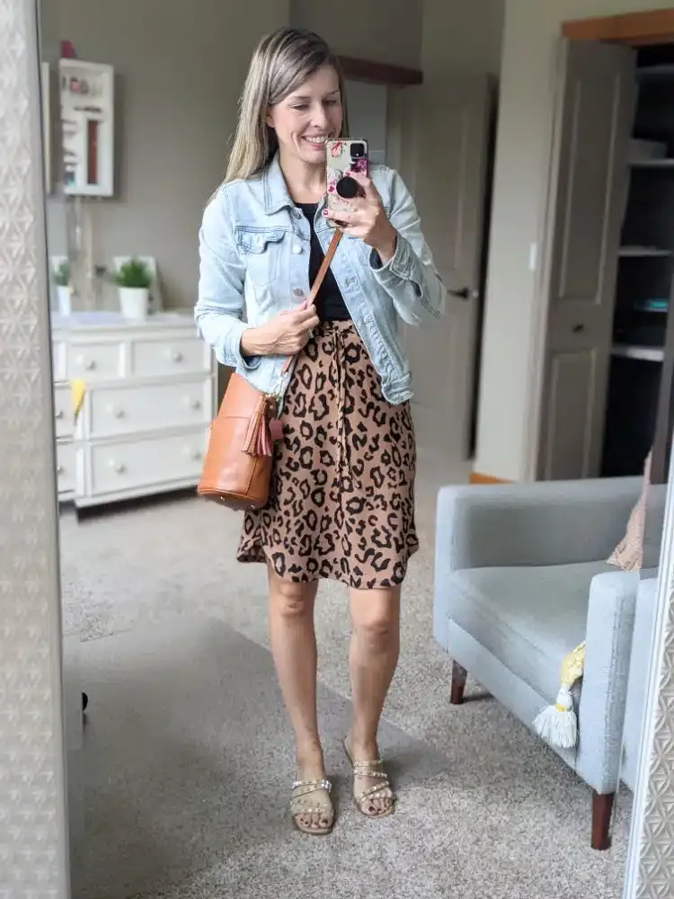Woman wearing a leopard print skirt with a black top and denim jacket in mirror selfie
