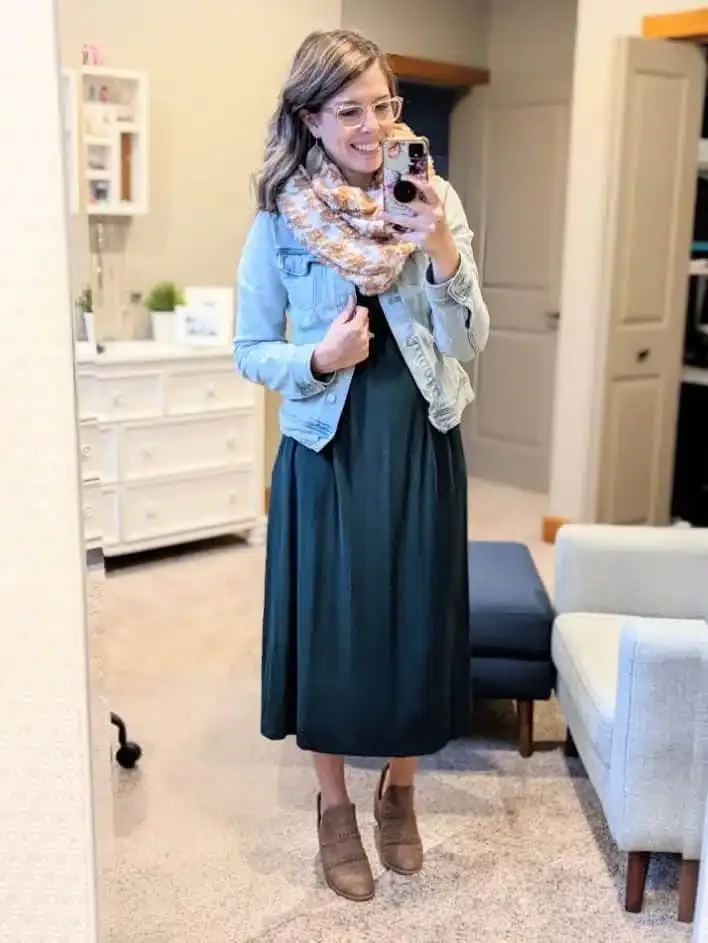 Woman wearing a green midi dress with a denim jacket, scarf, and ankle boots in a mirror selfie