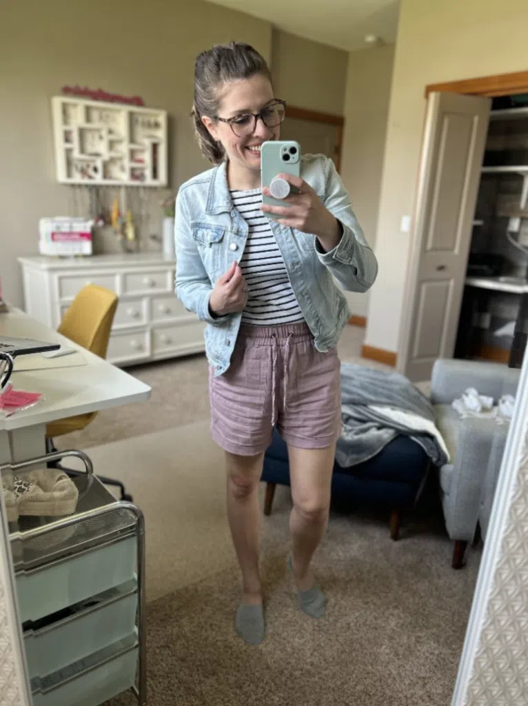 Woman wearing mauve shorts with a striped tee and denim jacket in a mirror selfie