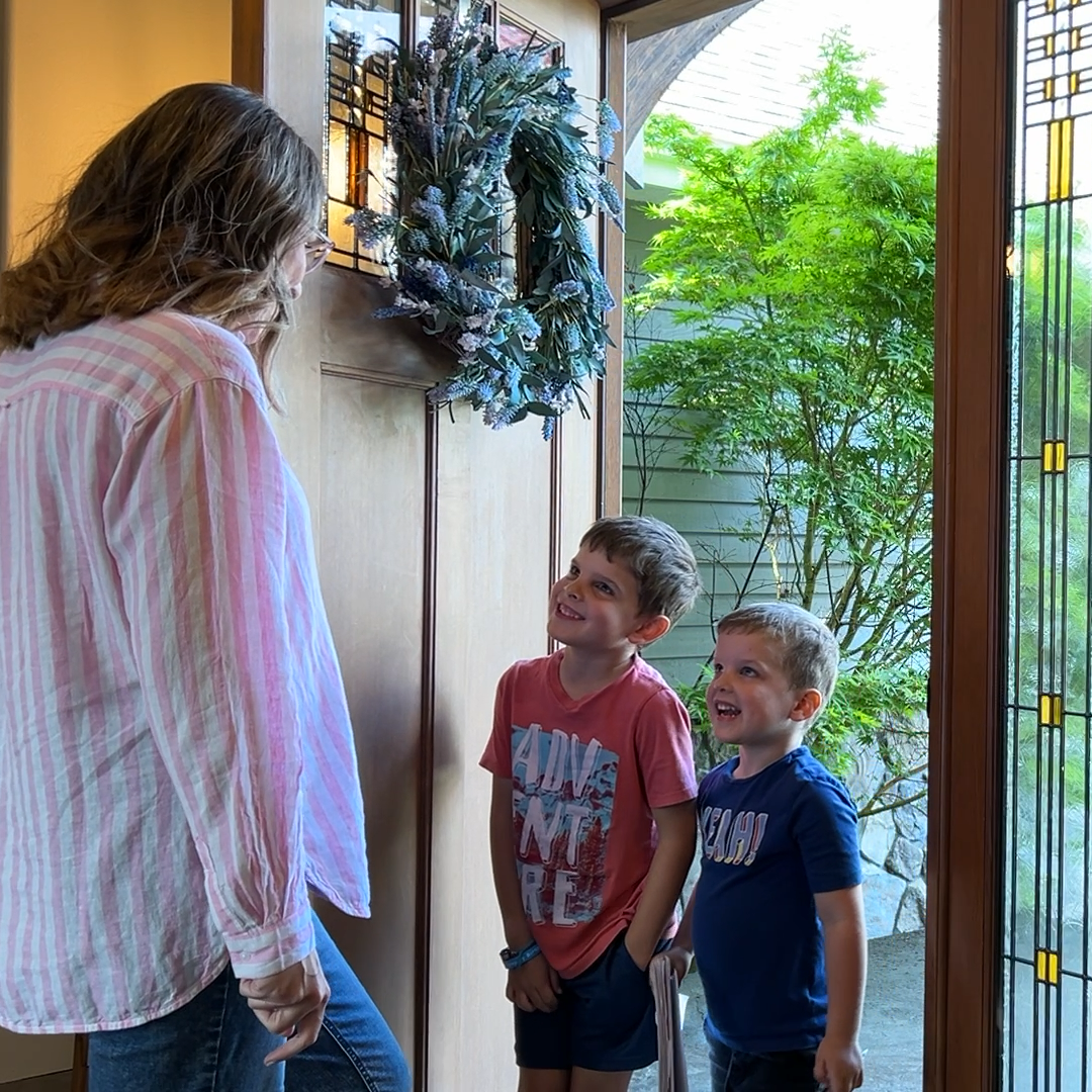 Mom dressed for the day smiling at kids by front door before leaving house