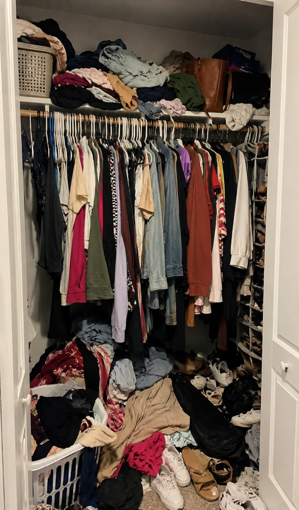 A cluttered closet packed with clothes on hangers, piles on the floor, and shoes scattered everywhere, showing the "before" of building a summer capsule wardrobe.